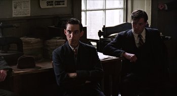 Movie still from “The Wind that Shakes the Barley” (2006), directed by Ken Loach – A man in a suit sitting in front of a window; Medium shot, Low angle