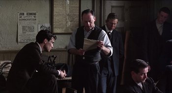 Movie still from “The Wind that Shakes the Barley” (2006), directed by Ken Loach – A group of men standing next to each other in a room; Medium shot, Over the shoulder angle