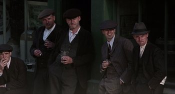 Movie still from “The Wind that Shakes the Barley” (2006), directed by Ken Loach – A group of men standing next to each other holding drinks; Medium shot, High angle