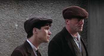 Movie still from “The Wind that Shakes the Barley” (2006), directed by Ken Loach – Two men in hats and suits standing next to each other; Close Up shot, Low angle