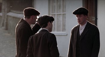 Movie still from “The Wind that Shakes the Barley” (2006), directed by Ken Loach – A group of men standing next to each other wearing hats; Medium shot, Over the shoulder angle