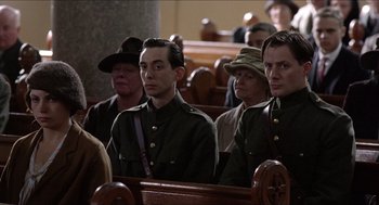 Movie still from “The Wind that Shakes the Barley” (2006), directed by Ken Loach – A group of people sitting in a row of pews; Medium shot, Low angle