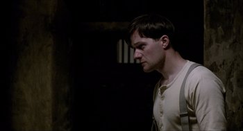 Movie still from “The Wind that Shakes the Barley” (2006), directed by Ken Loach – A man in a white shirt is standing in a dark room; Close Up shot, High angle