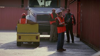 Movie still from “The Wire” (2002), created by David Simon – A man standing on a skateboard in front of a truck; Wide shot, Over the shoulder angle
