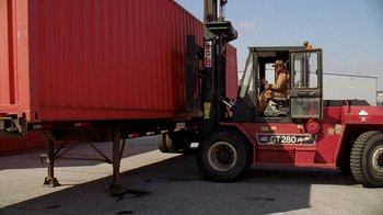 Movie still from “The Wire” (2002), created by David Simon – A man sitting on the back of a fork lift truck; Wide shot, Low angle