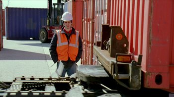 Movie still from “The Wire” (2002), created by David Simon – A man in an orange vest standing in front of a train; Medium shot, Low angle