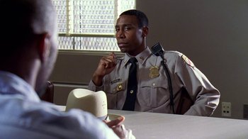 Movie still from “The Wire” (2002), created by David Simon – A police officer sitting at a table with a cowboy hat on; Close Up shot, Over the shoulder angle