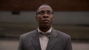 Movie still from “The Wire” (2002), created by David Simon – A man wearing a suit and bow tie; Close Up shot, Low angle