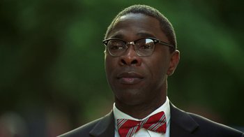 Movie still from “The Wire” (2002), created by David Simon – A person wearing glasses and a bow tie; Close Up shot, Low angle