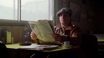 Movie still from “The Wire” (2002), created by David Simon – A man sitting at a table reading a newspaper; Medium shot, Low angle