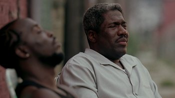 Movie still from “The Wire” (2002), created by David Simon – A man sitting next to another man with his eyes wide open; Close Up shot, Low angle