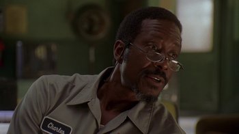 Movie still from “The Wire” (2002), created by David Simon – A person wearing glasses and a brown shirt; Close Up shot, Over the shoulder angle