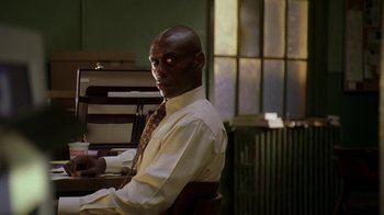 Movie still from “The Wire” (2002), created by David Simon – A man sitting at a desk in front of an open window; Close Up shot, Low angle