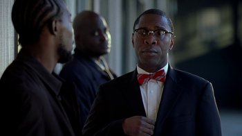 Movie still from “The Wire” (2002), created by David Simon – A man in a suit and bow tie standing next to two other men; Close Up shot, Over the shoulder angle