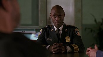 Movie still from “The Wire” (2002), created by David Simon – A police officer sitting at a table with his hands crossed; Close Up shot, Over the shoulder angle