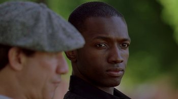 Movie still from “The Wire” (2002), created by David Simon – A man in a black shirt and a man in a gray hat; Close Up shot, Over the shoulder angle