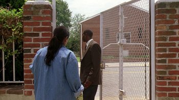 Movie still from “The Wire” (2002), created by David Simon – A man and a woman standing in front of a fence; Wide shot, Over the shoulder angle
