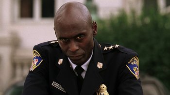 Movie still from “The Wire” (2002), created by David Simon – A man in a police uniform sitting in front of a building; Close Up shot, Low angle