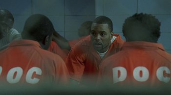 Movie still from “The Wire” (2002), created by David Simon – A group of men in orange jumpsuits in a room; Medium shot, Over the shoulder angle