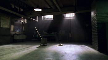 Movie still from “The Wire” (2002), created by David Simon – A room that has a chair in the middle of the floor; Extreme Wide shot, High angle