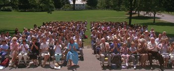 Movie still from “The Witches of Eastwick” (1987), directed by George Miller – A large group of people sitting in chairs in a field; Wide shot, High angle