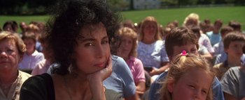 Movie still from “The Witches of Eastwick” (1987), directed by George Miller – A group of women sitting in a row and one woman is looking at the camera; Close Up shot, Over the shoulder angle