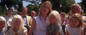 Movie still from “The Witches of Eastwick” (1987), directed by George Miller – A woman and a child in a crowd of onlookers at an outdoor event; Close Up shot, Low angle