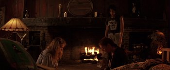 Movie still from “The Witches of Eastwick” (1987), directed by George Miller – A group of people sitting in front of a fire place; Wide shot, High angle