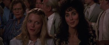 Movie still from “The Witches of Eastwick” (1987), directed by George Miller – Two women sitting next to each other in front of an audience; Close Up shot, Over the shoulder angle