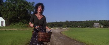 Movie still from “The Witches of Eastwick” (1987), directed by George Miller – A woman riding a bike down a dirt road; Medium shot, Low angle