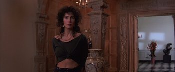 Movie still from “The Witches of Eastwick” (1987), directed by George Miller – A woman standing next to a vase in a room; Medium shot, Low angle