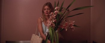 Movie still from “The Witches of Eastwick” (1987), directed by George Miller – A woman sitting next to a plant with pink flowers in it; Medium shot, Low angle