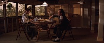 Movie still from “The Witches of Eastwick” (1987), directed by George Miller – A man sitting at a table with a plate of food on top of it; Wide shot, Over the shoulder angle