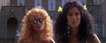 Movie still from “The Witches of Eastwick” (1987), directed by George Miller – Two women standing next to each other in front of a building; Close Up shot, Low angle