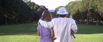 Movie still from “The Witches of Eastwick” (1987), directed by George Miller – Two people standing in the grass hugging each other; Wide shot, Low angle