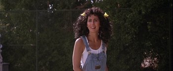 Movie still from “The Witches of Eastwick” (1987), directed by George Miller – A woman in a white shirt and blue jean overalls; Medium shot, Over the shoulder angle