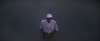 Movie still from “The Witches of Eastwick” (1987), directed by George Miller – A man wearing a white hat and holding a pair of shoes; Wide shot, Overhead angle