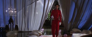 Movie still from “The Witches of Eastwick” (1987), directed by George Miller – A man in a red suit stands in front of a white curtain; Wide shot, Low angle