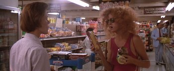 Movie still from “The Witches of Eastwick” (1987), directed by George Miller – A woman with curly hair is looking at a box of bananas; Medium shot, Over the shoulder angle