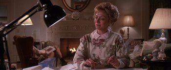 Movie still from “The Witches of Eastwick” (1987), directed by George Miller – An older woman sitting in front of a fireplace; Medium shot, Low angle