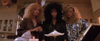 Movie still from “The Witches of Eastwick” (1987), directed by George Miller – A group of women standing next to each other in front of a candle; Medium shot, Low angle