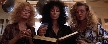 Movie still from “The Witches of Eastwick” (1987), directed by George Miller – A woman holding a drink and reading a book; Close Up shot, Low angle