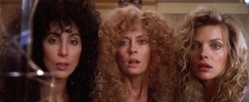 Movie still from “The Witches of Eastwick” (1987), directed by George Miller – A woman with long , curly hair is standing next to another woman with long , curly hair in front of a mirror; Close Up shot, Low angle