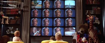 Movie still from “The Witches of Eastwick” (1987), directed by George Miller – Two people sitting in front of a television screen; Medium shot, High angle