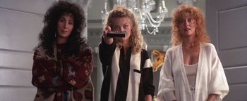 Movie still from “The Witches of Eastwick” (1987), directed by George Miller – A group of women standing next to each other holding a remote control; Medium shot, Low angle