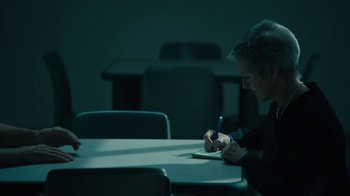 Movie still from “The Wizard of Lies” (2017), directed by Barry Levinson – A person sitting at a table writing on a piece of paper; Medium shot, High angle