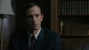 Movie still from “The Wizard of Lies” (2017), directed by Barry Levinson – A man wearing a suit and tie in a dark room; Close Up shot, Over the shoulder angle