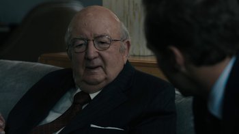 Movie still from “The Wizard of Lies” (2017), directed by Barry Levinson – An older man wearing glasses and a suit and tie; Close Up shot, Over the shoulder angle