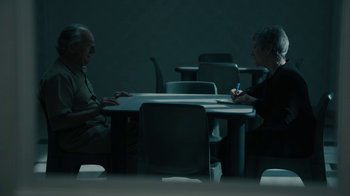 Movie still from “The Wizard of Lies” (2017), directed by Barry Levinson – Two people sitting at a table in a dark room; Wide shot, Over the shoulder angle
