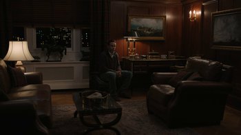 Movie still from “The Wizard of Lies” (2017), directed by Barry Levinson – A man sitting on a chair in a living room; Wide shot, High angle